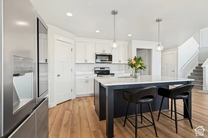 Kitchen featuring a central island with white countertop, pendant lighting, white cabinetry, and stainless steel appliances