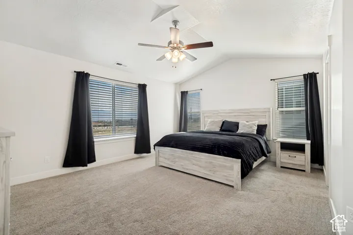 Vaulted ceiling, ceiling fan, large windows, light-colored walls, and carpet flooring