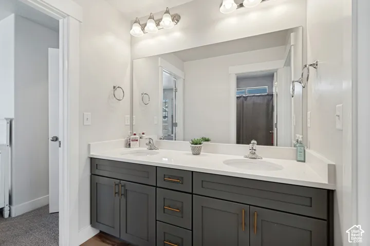 Dual vanity with quartz countertops, undermount sinks, gray shaker-style cabinetry, and brushed gold hardware
