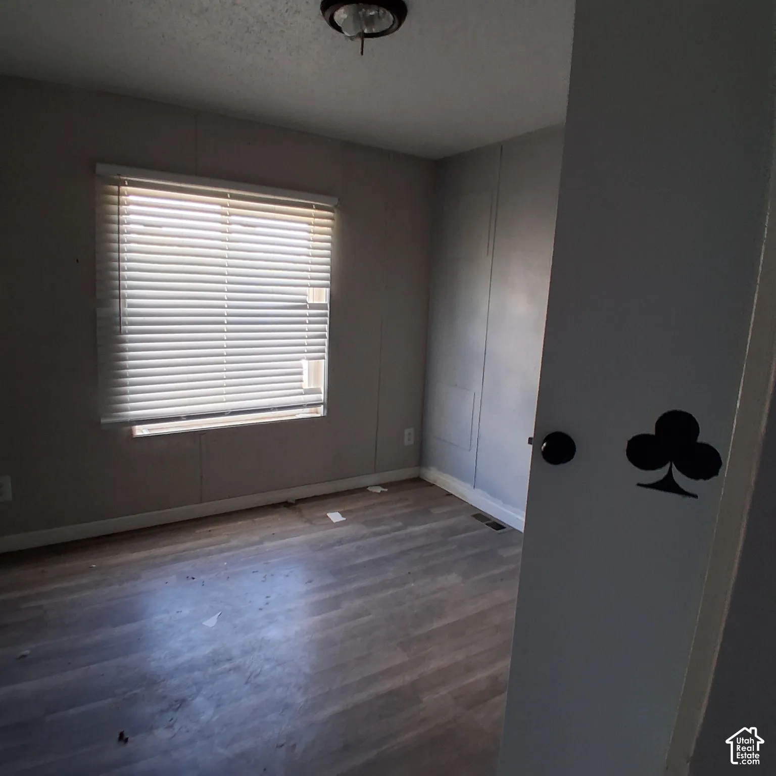 Room featuring wood-finish flooring, a large window with horizontal blinds, and a circular flush-mount ceiling light fixture