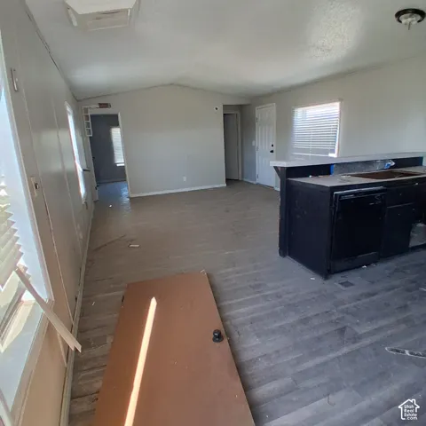 Interior space featuring wood-finish flooring, a kitchen peninsula with a black finish, and multiple windows with horizontal blinds