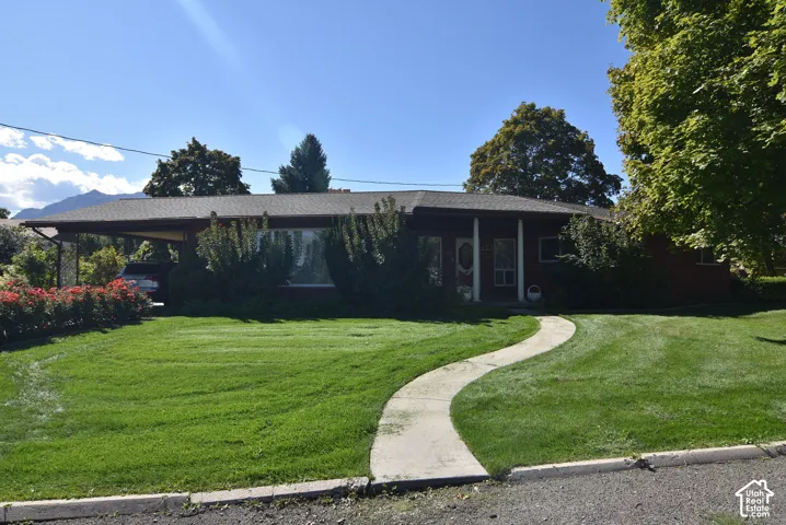 Single-story brick exterior featuring an attached carport, covered front porch with support columns, and concrete walkway set within a lawn with mature landscaping