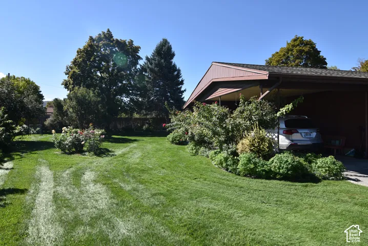 Spacious lot featuring a manicured lawn, established landscaping, mature trees, and an attached carport