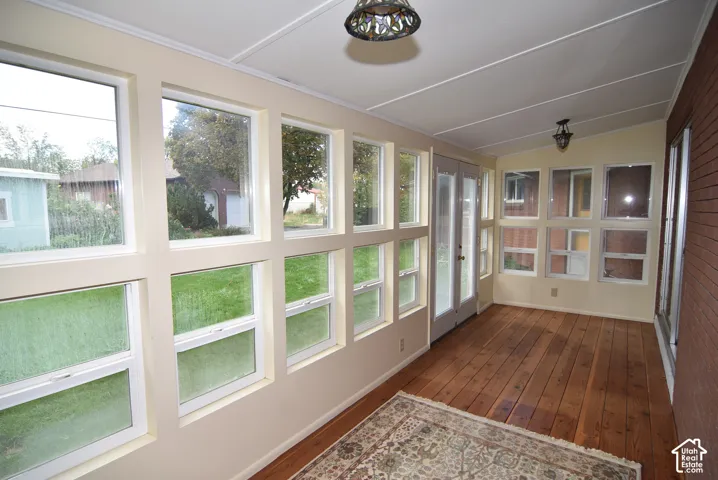 Enclosed sunroom featuring expansive windows, wood-finish flooring, brick wall detailing, and dual glass-panel entry doors