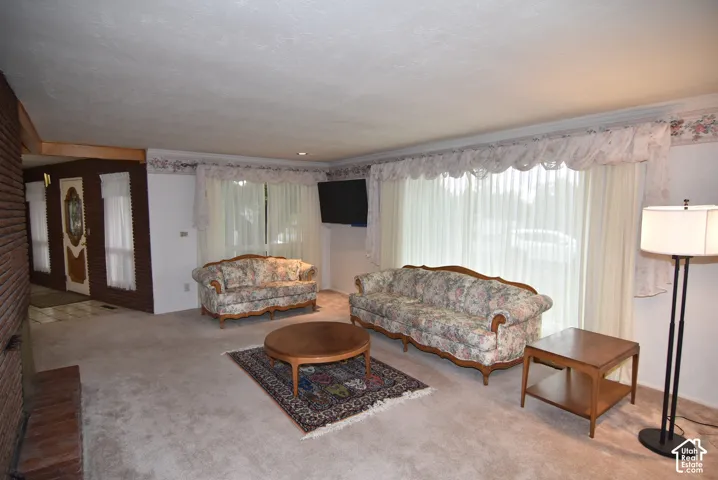 Floor-to-ceiling windows with crown molding, brick fireplace surround, decorative wood door with glass inlay, and wall-to-wall carpeting