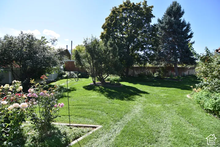 Expansive lawn, mature trees, tiered garden beds, and perimeter wood fencing
