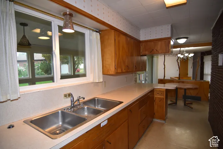 Kitchen featuring wood cabinetry, stainless steel dual-basin sink, solid-surface countertops, and a decorative brick accent wall
