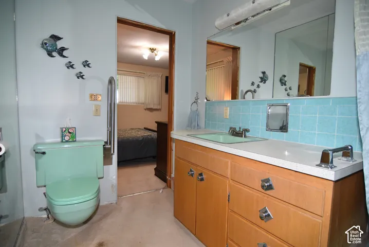 Bathroom featuring a wood-finish vanity, integrated sink basin, solid-surface countertop, full-width mirror with overhead lighting, and blue tile backsplash