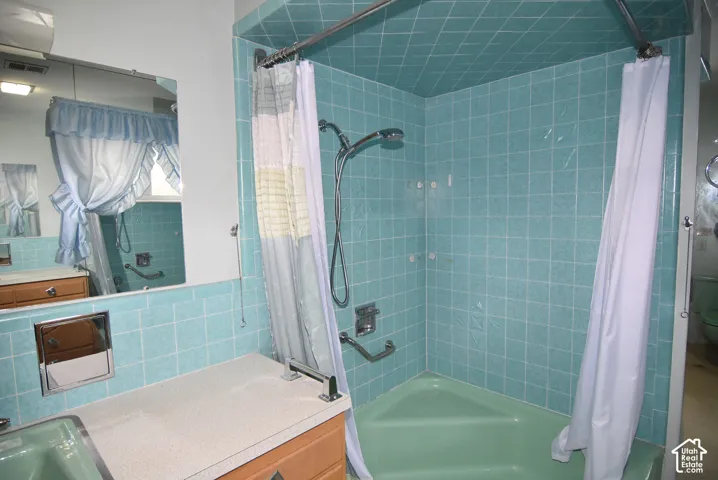 Bathroom featuring a corner soaking tub, ceramic tile surround, integrated vanity countertop with sink, and wall-mounted hand shower fixture