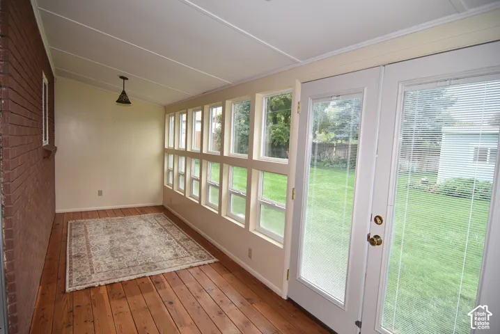 Enclosed sunroom featuring exposed brick walling, wood-finish flooring, a wall of multi-pane windows, and double glass-panel doors with integrated blinds