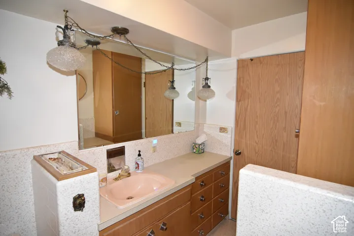 Vanity featuring integrated sink, expansive countertop, ample cabinetry storage, wall-mounted mirror, and multi-light pendant fixture