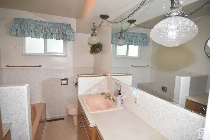 Bathroom featuring a wood-finish vanity with a molded basin, expansive wall-mounted mirror, terrazzo-style tile wainscoting, and pendant lighting