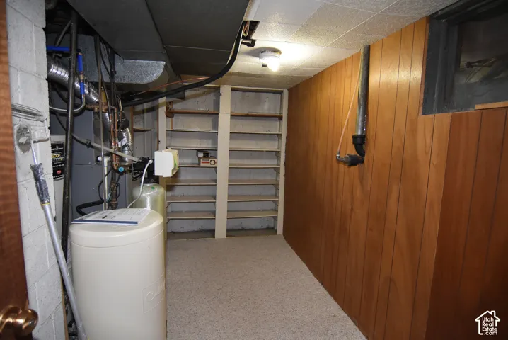 Utility area featuring wood-panel wall cladding, built-in shelving, concrete block walls, and a dedicated water filtration system