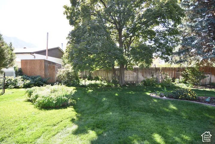 Backyard featuring a manicured lawn, established shade trees, wood-slat fencing, and garden beds with stone curbing