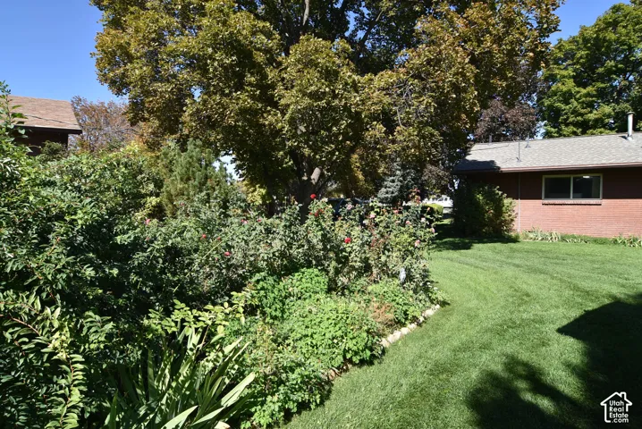 Spacious backyard featuring a manicured lawn, established landscaping, mature trees, and red brick exterior finish