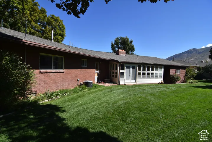 Exterior featuring red brick construction, a multi-pane sunroom with double doors, and a composition shingle roof, set against a backdrop of mountain scenery