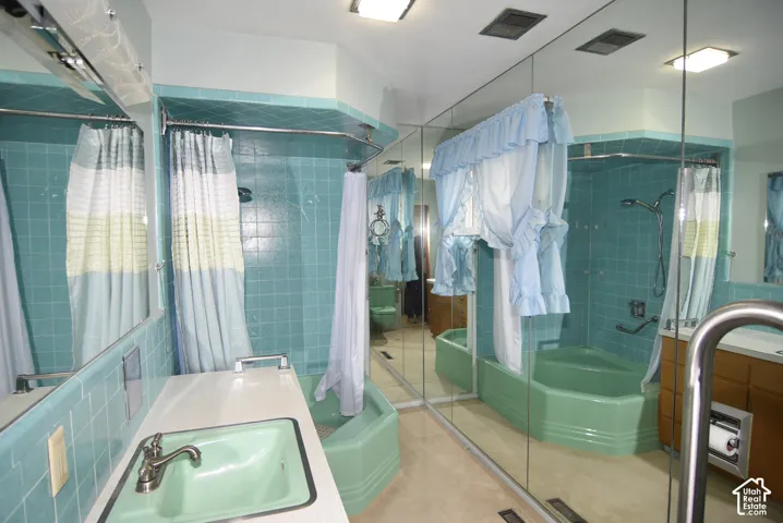 Full-wall mirror, tiled surround, corner tub, and wood-finish vanity cabinetry