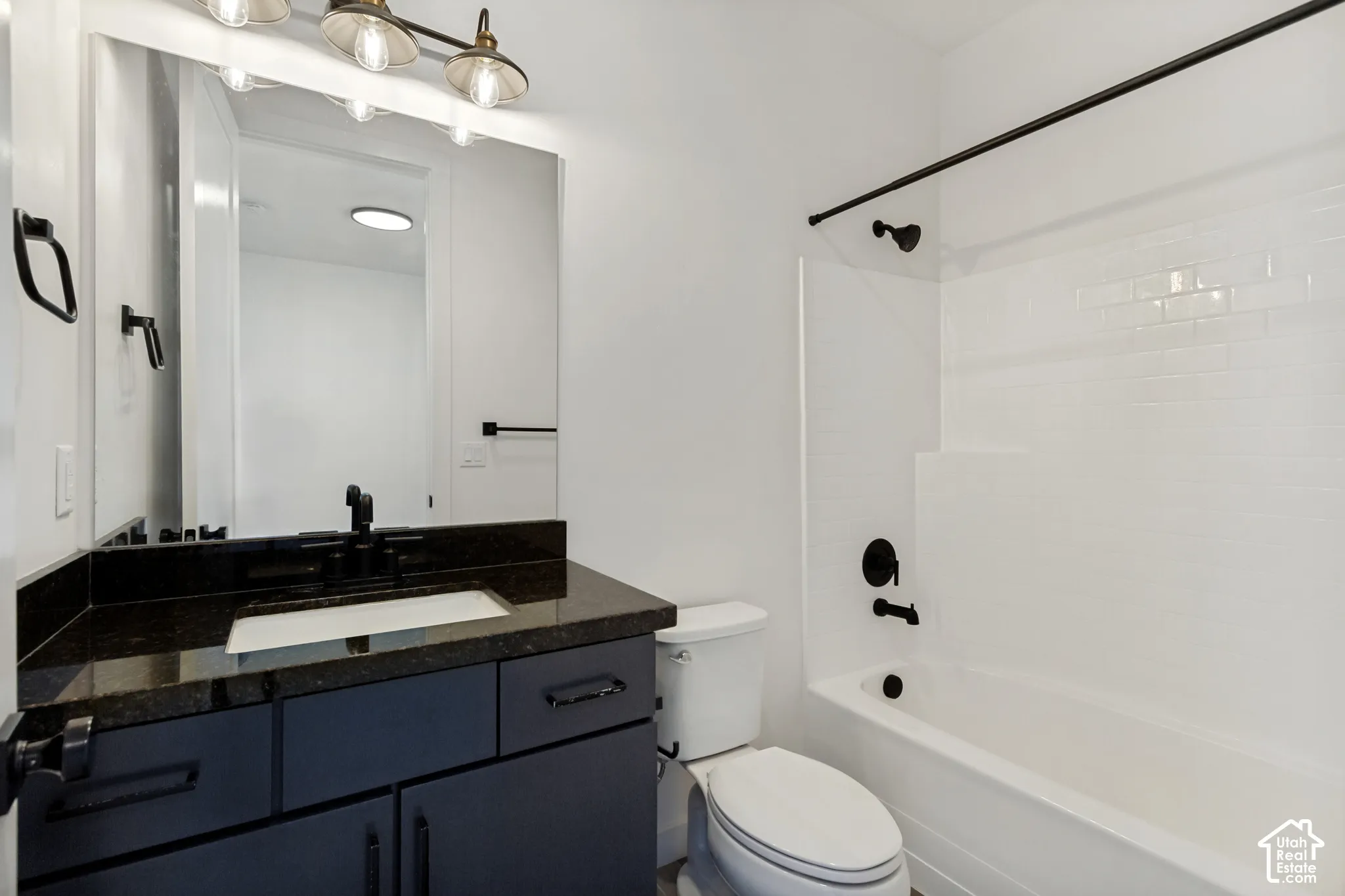 Dark-finish vanity with a stone countertop, under-mount sink, matte black fixtures, large vanity mirror, and a tub-shower combination with white subway-style tile surround