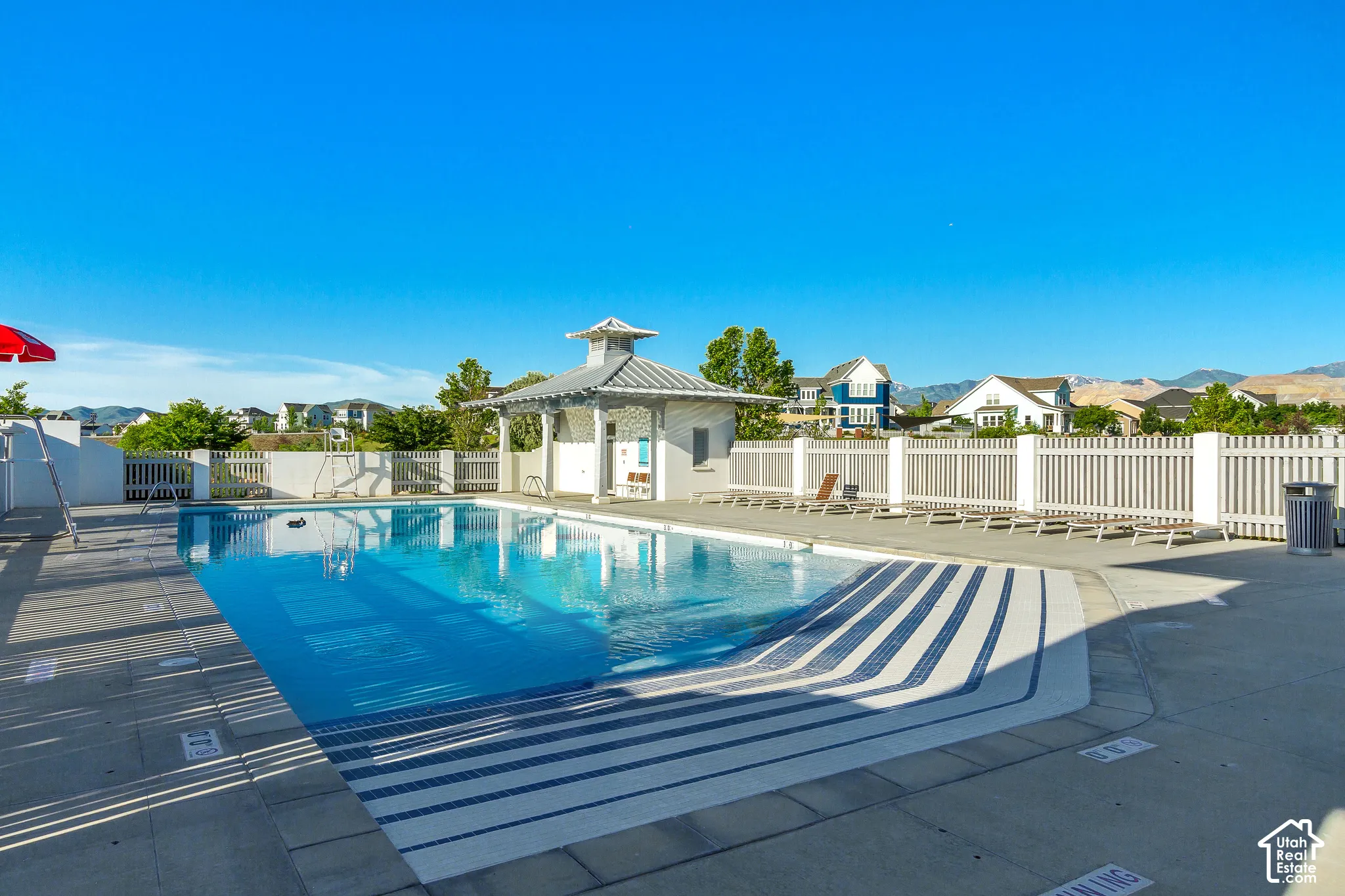 Swimming pool featuring a concrete deck, built-in steps, and a covered pavilion with metal roofing, enclosed by perimeter fencing