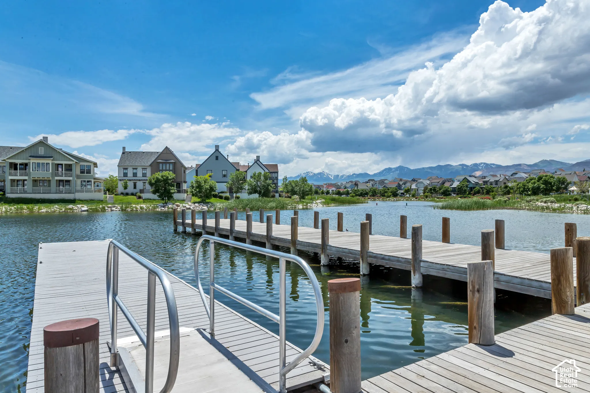 Private wooden dock featuring metal handrails and reinforced piling supports, set upon a community water feature with mountain backdrops
