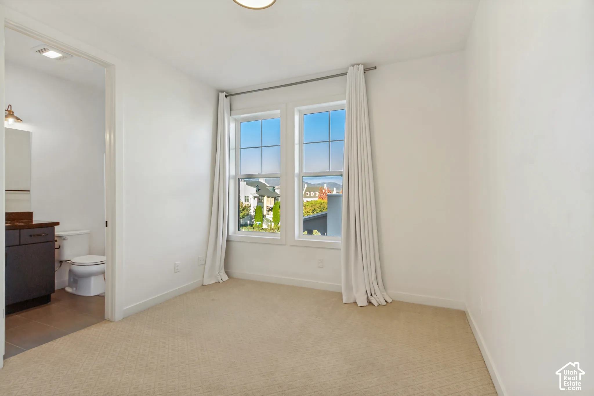Room featuring neutral carpeting, dual-pane windows with mountain and neighborhood scenery, and a doorway opening to a bathroom with a dark-finish vanity