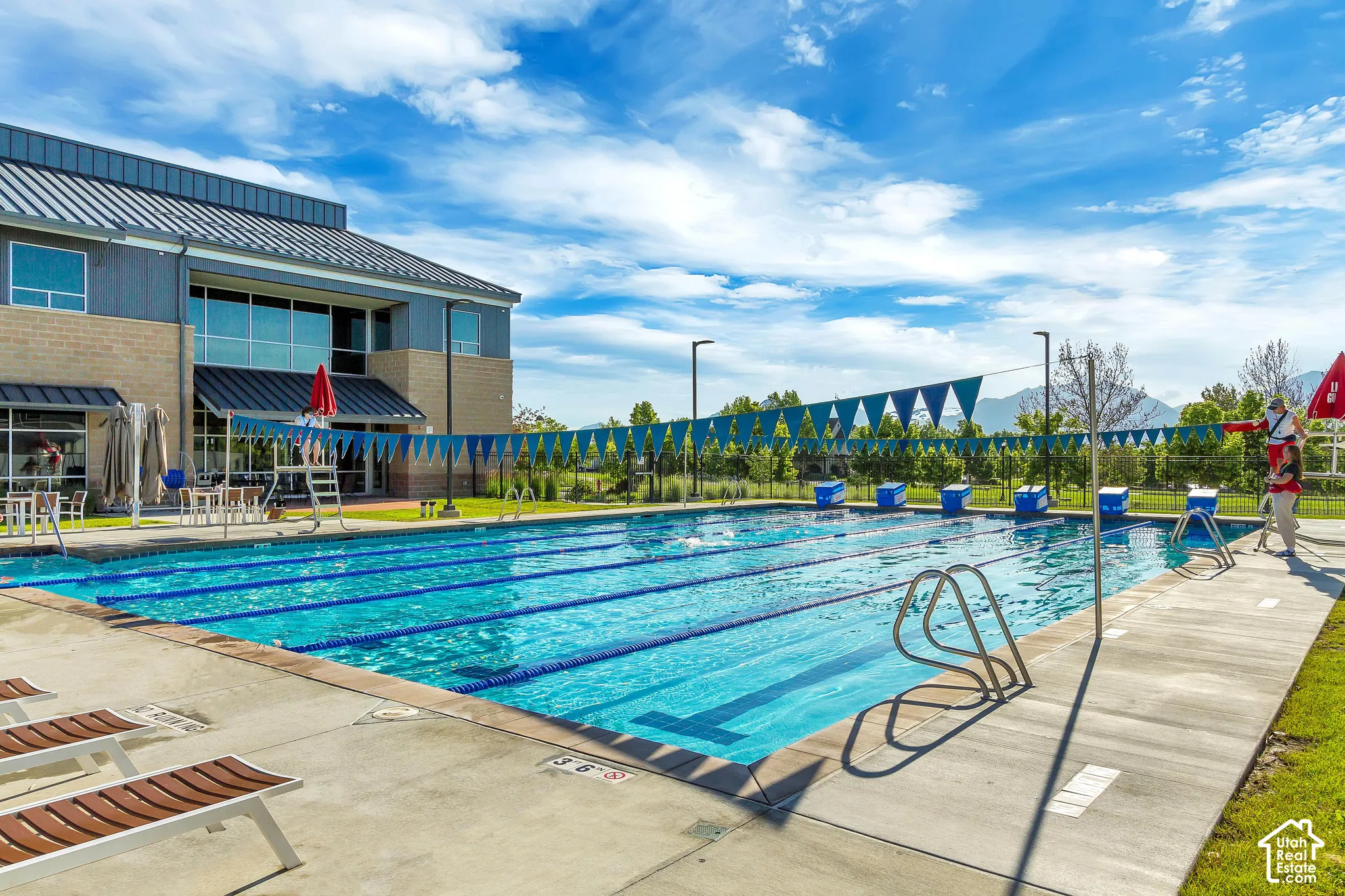 Multi-lane lap pool featuring concrete decking, metal starting blocks, lane dividers, and a metal-roofed structure with floor-to-ceiling windows