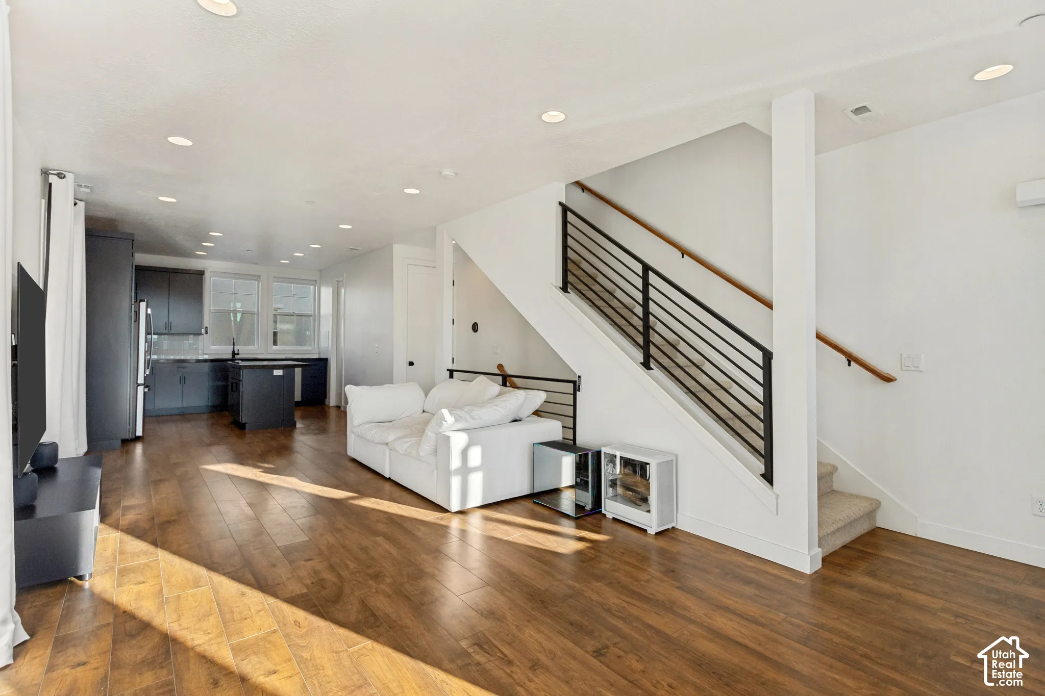 Open-concept interior featuring wood-finish flooring, recessed lighting, and a staircase with a modern horizontal metal railing and wooden handrail