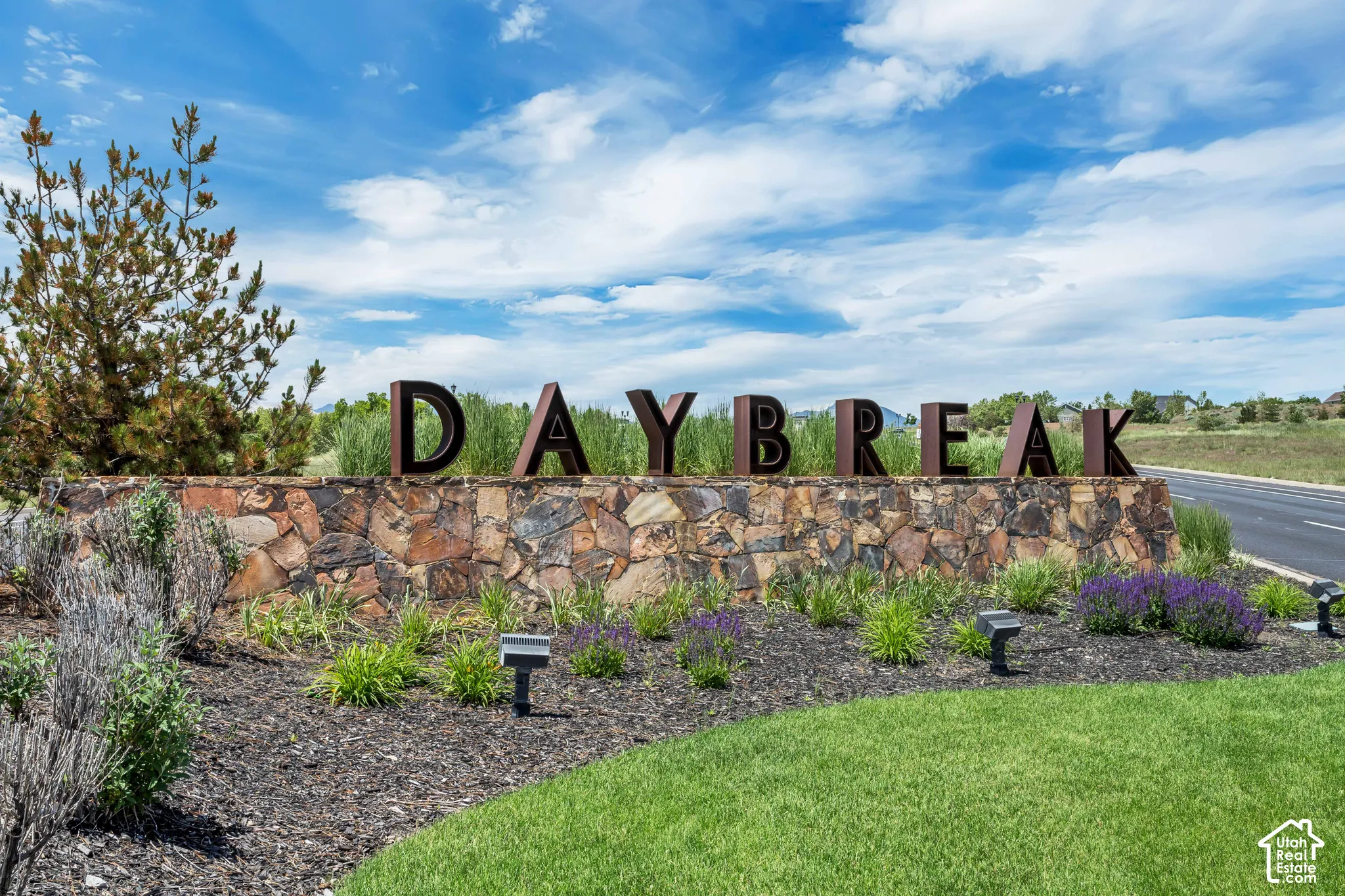 Community entrance featuring prominent metal signage, natural stone masonry, manicured lawn, and professional landscaping