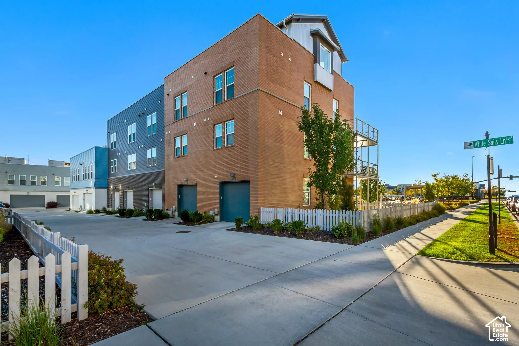 Multi-level exterior featuring a brick and composite siding facade, attached multi-car garages, metal balcony railings, and a fenced perimeter