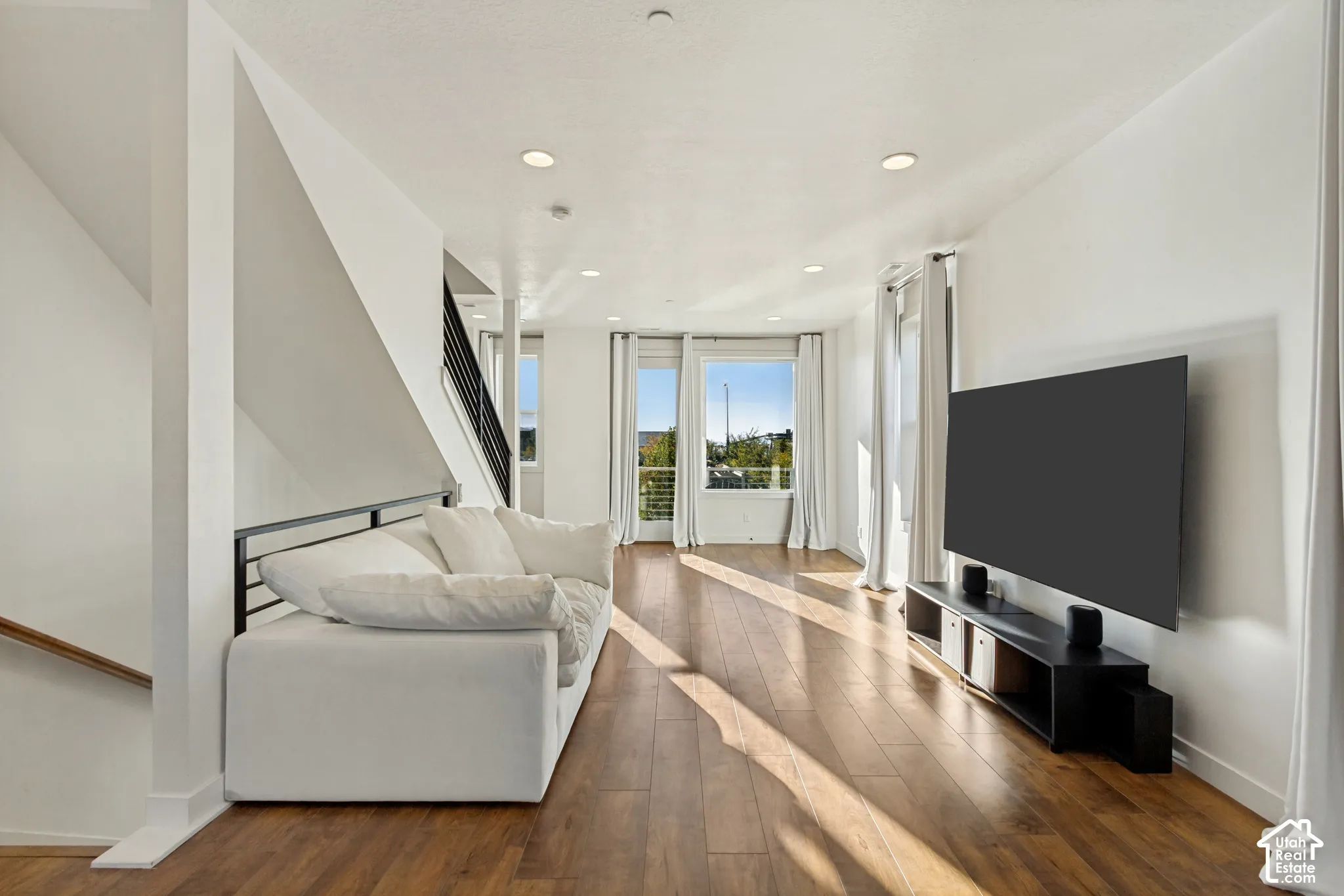 Living area featuring wood-finish flooring, recessed lighting, and a metal stair railing