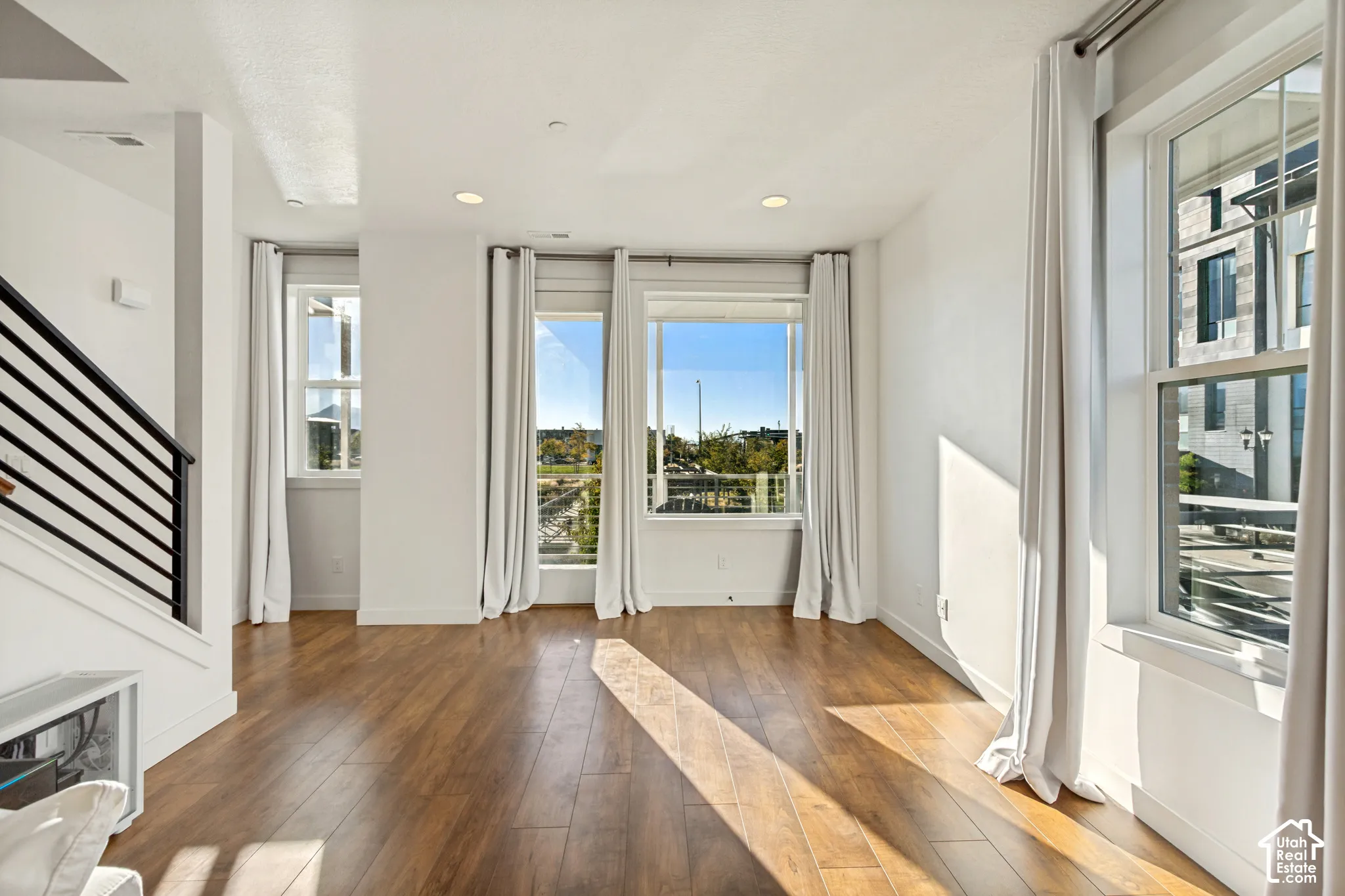 Open-concept interior featuring wood-finish flooring, recessed lighting, expansive windows, and a staircase with a metal railing