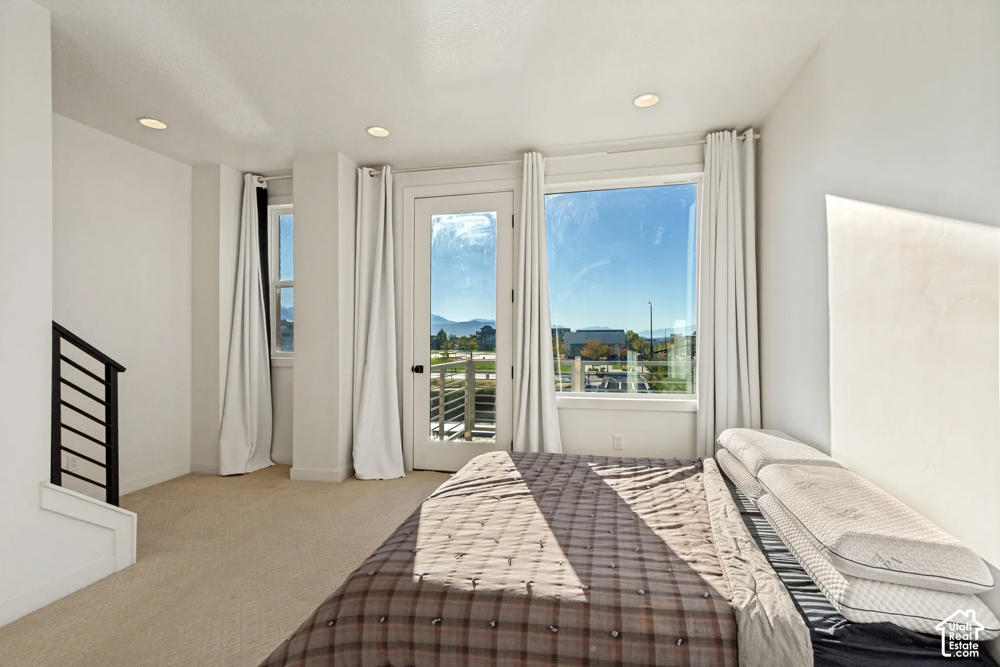 Carpeted room featuring floor-to-ceiling windows, a glass-panel exterior door, recessed ceiling lighting, and a metal-railing staircase