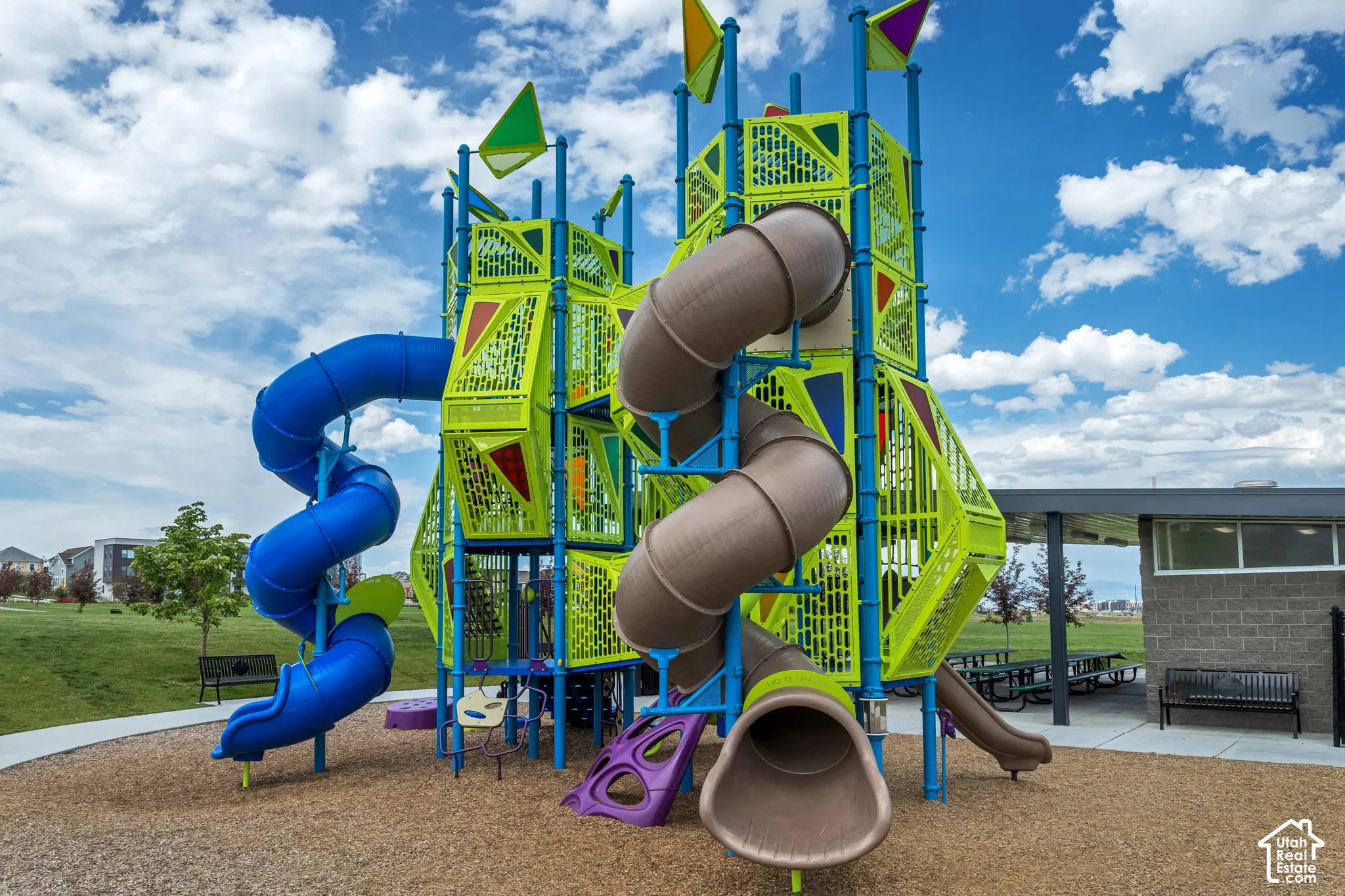 Multi-level playground structure featuring dual spiral slides, a covered outdoor pavilion with concrete flooring, and metal seating benches
