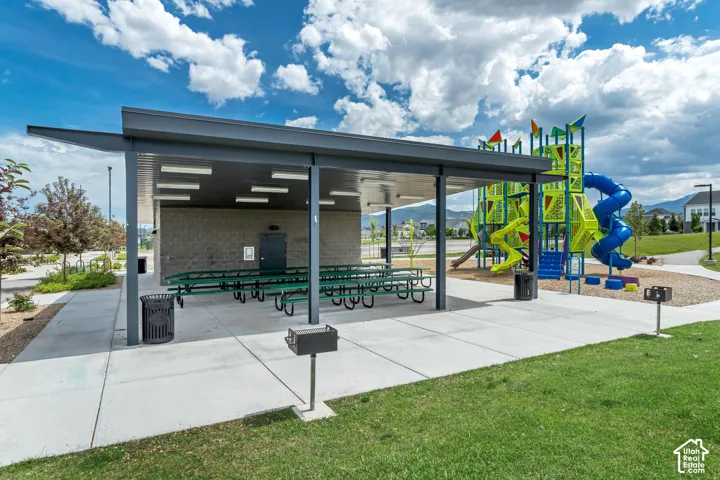 Covered pavilion featuring a concrete patio, integrated lighting, metal grills, and a multi-level playground structure