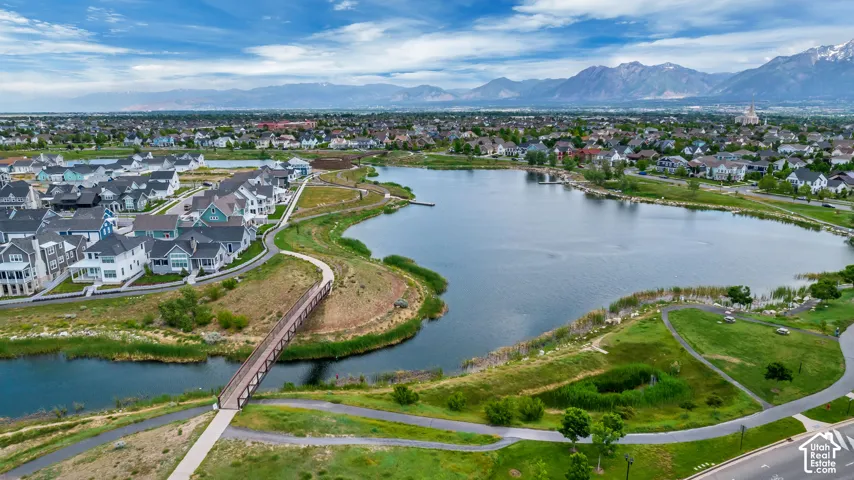 Aerial perspective featuring a large lake, pedestrian bridge, paved pathways, and mountain backdrop