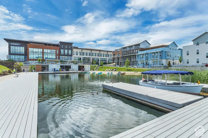 Waterfront recreational area featuring composite decking, floating boat slips, manicured lawn, and multi-story commercial and residential buildings