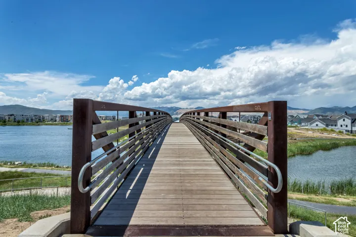 Pedestrian bridge featuring wood decking, metal railings, and a concrete foundation, overlooking a lake with mountain scenery