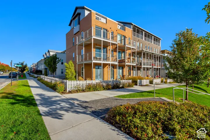 Multi-story brick exterior featuring stacked metal balconies, a white picket fence, and concrete walkways