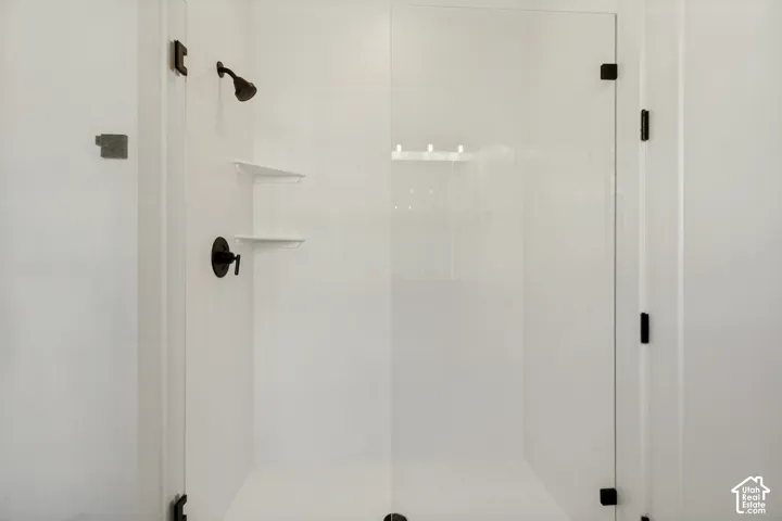Walk-in shower featuring a frameless glass door, matte black hardware, built-in shelving, and a wall-mounted shower head