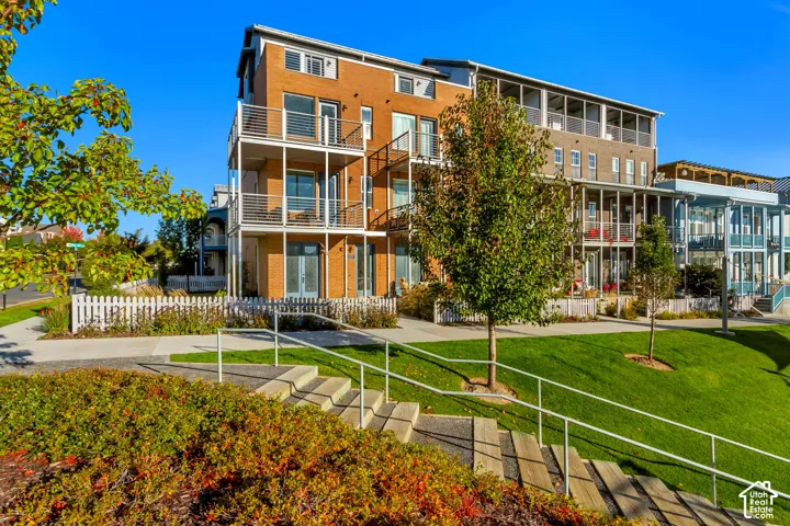 Multi-story brick exterior featuring stacked cantilevered balconies with horizontal metal railing, white picket fencing, and concrete stairs with metal handrails