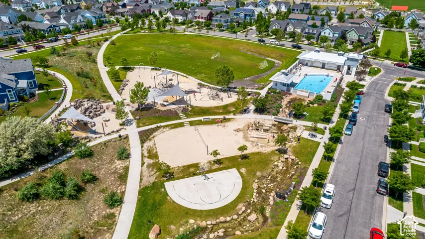 Aerial perspective of recreational area including an outdoor swimming pool with pool house, open grass fields, sand court, and concrete half-court basketball area