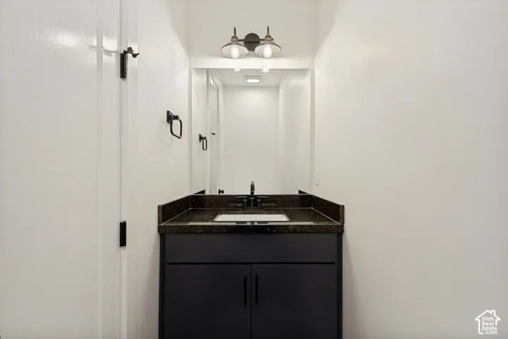 Dark-finish vanity with a rectangular under-mount sink, stone-surface countertop, dual-light wall fixture, and matte black hardware