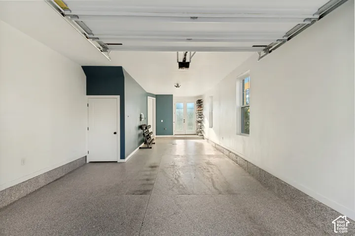 Finished garage with epoxy flooring, neutral wall paint, two interior doors, and glass-paneled double exterior doors