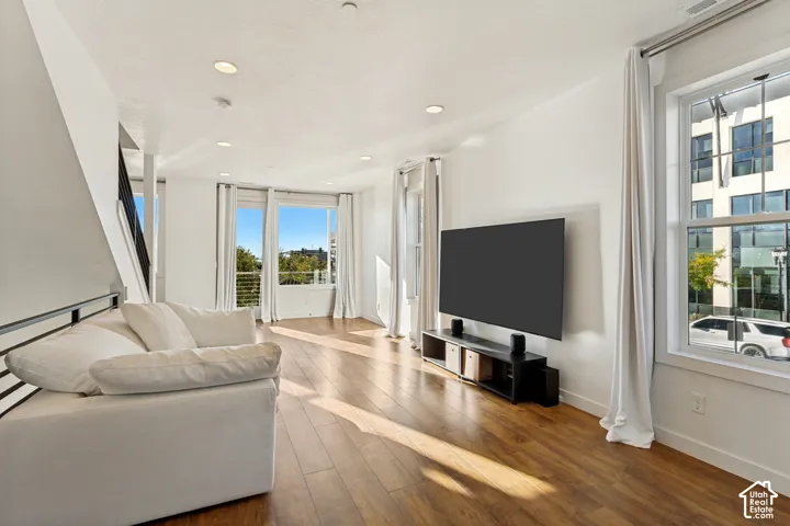 Open-concept interior featuring wood-finish flooring, recessed lighting, expansive windows, and a metal-railed staircase