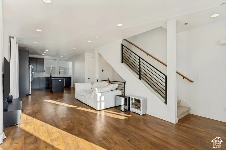Open-concept interior featuring wood-finish flooring, recessed lighting, and a staircase with a modern horizontal metal railing and wooden handrail