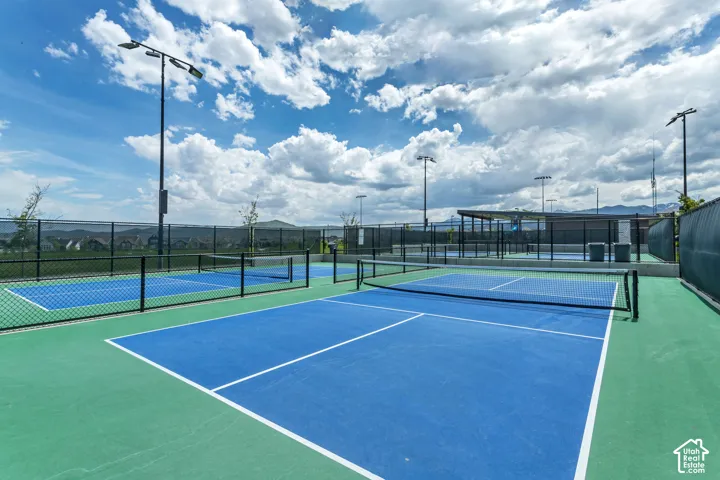 Recreational court area featuring multiple blue and green pickleball courts, black chain-link perimeter fencing, and overhead stadium-style lighting