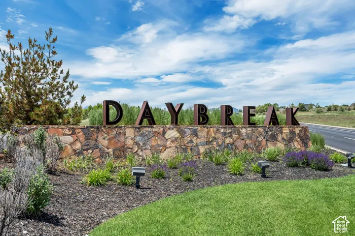 Community entrance featuring prominent metal signage, natural stone masonry, manicured lawn, and professional landscaping