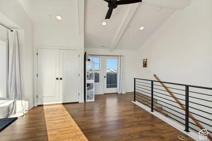 Vaulted ceiling featuring exposed beams, wood-finish flooring, matte black ceiling fan, and staircase with horizontal metal railing