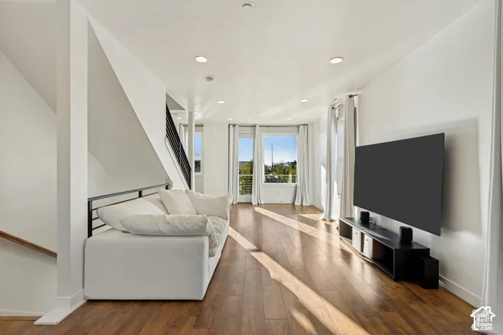 Living area featuring wood-finish flooring, recessed lighting, and a metal stair railing