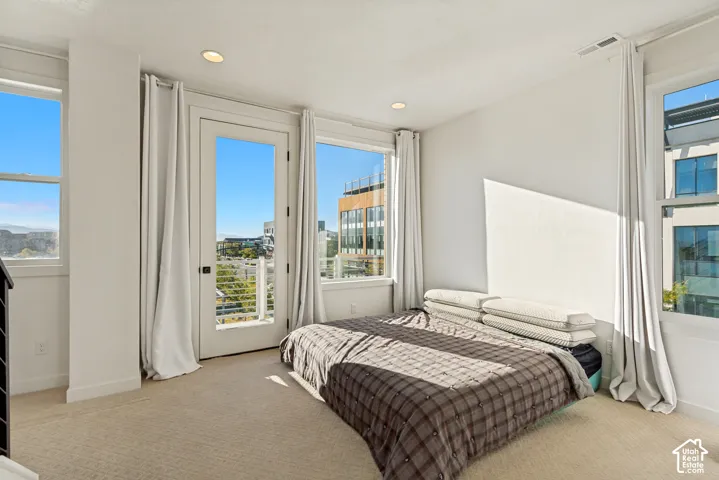 Neutral-toned carpeting, multiple large windows providing natural light, recessed lighting, and a glass-paneled door opening to a balcony